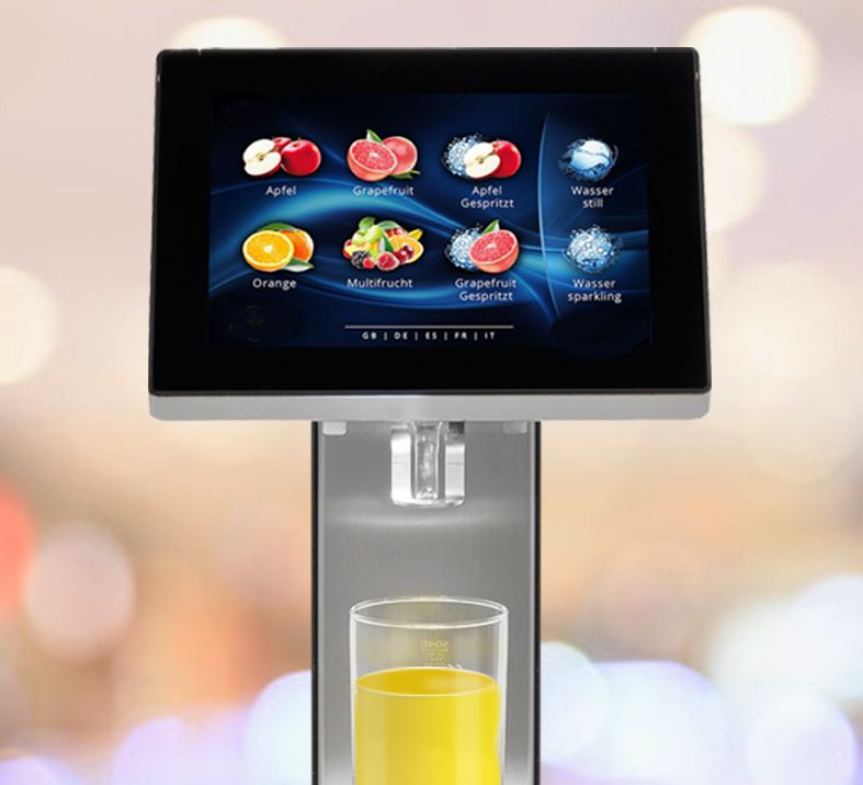 trinkForm® Getränkeautomat zeigt vielfältige Getränkeauswahl auf dem Touchscreen, serviert frischen Orangensaft